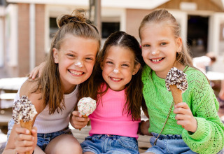 Tres niñas sonrientes comen helado en un alojamiento glamping, con helado en la nariz y rostros felices.