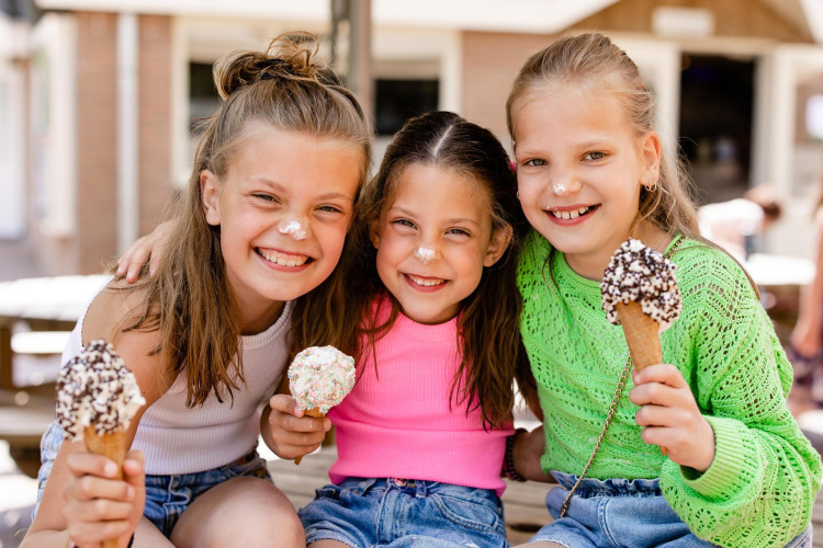 Tres niñas sonrientes comen helado en un alojamiento glamping, con helado en la nariz y rostros felices.