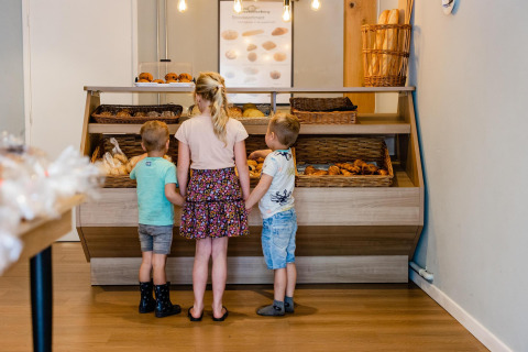 Tres niños eligen bollería en la vitrina de una panadería dentro de un alojamiento glamping moderno.