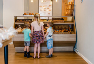 Tres niños eligen bollería en la vitrina de una panadería dentro de un alojamiento glamping moderno.