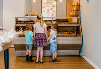 Drie kinderen staan bij het broodrek in een glampingverblijf en kiezen versgebakken broodjes uit.