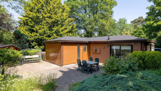 Chalet en bois chaleureux avec terrasse, table et chaises, entouré de verdure à Heide Lodge, Het Verscholen Dorp.