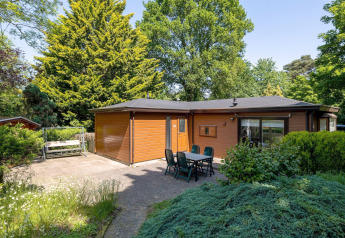 Hyggelig lodge i træ med terrasse, havebord og masser af grønne træer, Heide lodge i Bungalowpark Het Verscholen Dorp.