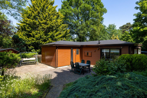 Chalet en bois chaleureux avec terrasse, table et chaises, entouré de verdure à Heide Lodge, Het Verscholen Dorp.