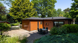 Gemütliche Holzhütte mit Terrasse, Gartentisch, umgeben von Bäumen, Heide Lodge im Het Verscholen Dorp, Niederlande.