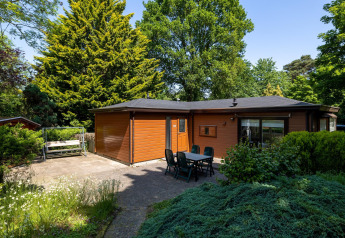 Acogedora cabaña de madera con terraza, mesa y sillas, rodeada de naturaleza, en Heide Lodge, Het Verscholen Dorp.