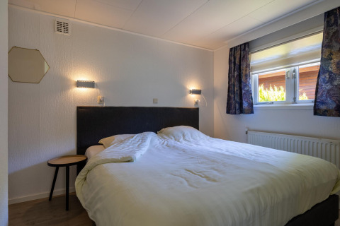 Dormitorio en Heide Lodge, Bungalowpark Het Verscholen Dorp, Países Bajos, con cama doble y ventana.