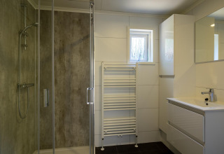 Baño moderno con ducha acristalada, lavabo, espejo y radiador toallero en Heide lodge en Het Verscholen Dorp, Países Bajos.