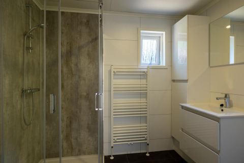 Moderne badkamer met douche, lavabo, spiegel en handdoekradiator in Heide lodge in Het Verscholen Dorp, Nederland.