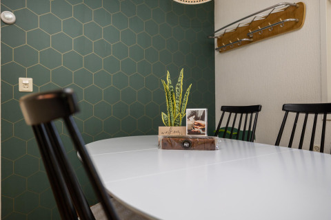 Comedor moderno en Heide lodge con mesa blanca, sillas negras y pared de azulejos hexagonales verdes.