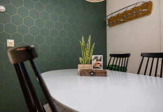 Comedor moderno en Heide lodge con mesa blanca, sillas negras y pared de azulejos hexagonales verdes.