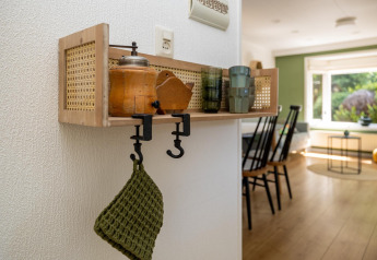 Estante de pared con utensilios de cocina y paño verde en interior luminoso del Heide lodge, Países Bajos.