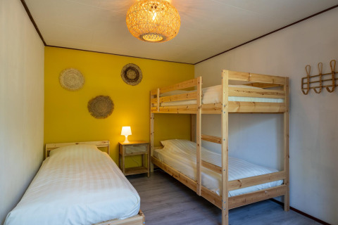 Dormitorio en Heide lodge en Bungalowpark Het Verscholen Dorp, Países Bajos, con cama individual y litera.