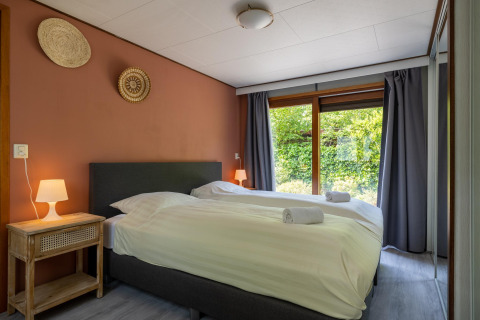 Moderne slaapkamer in Heide lodge, Het Verscholen Dorp, met twee bedden en uitzicht op de tuin.
