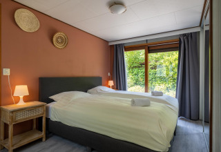 Moderne slaapkamer in Heide lodge, Het Verscholen Dorp, met twee bedden en uitzicht op de tuin.