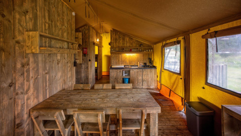Interior de una tienda glamping tipo safari en Holiday Park Duinhoeve, Países Bajos, con muebles de madera.