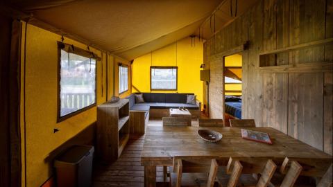 Interior de una tienda safari Glamping Lodge en Holiday Park Duinhoeve, con muebles de madera y sofá.