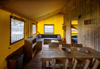 Interieur van een Glamping Lodge safaritent in Holiday Park Duinhoeve, met houten meubilair en een zetel.
