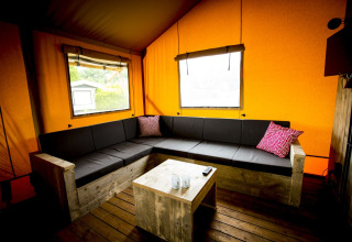 Binnenzicht van een safari tent Glamping Lodge met hoekbank, houten tafel en oranje doeken muren.