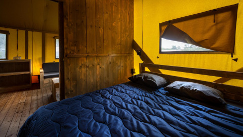 Interior de una tienda glamping tipo safari con suelo y muebles de madera y ropa de cama azul en Duinhoeve.