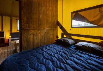 Interno di una tenda safari glamping con pavimento in legno, arredi rustici e letto blu al Duinhoeve.