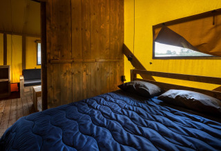 Innenansicht eines Safari-Glampingzeltes mit Holzboden, Möbeln und blauem Bett bei Holiday Park Duinhoeve.