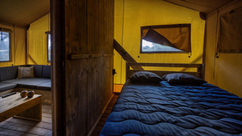 Vista interior de una tienda safari Glamping Lodge con cama y sala en Holiday Park Duinhoeve, Países Bajos.