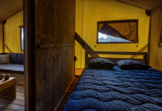 Binnenzicht van een Glamping Lodge safaritent met bed en zithoek in Holiday Park Duinhoeve.