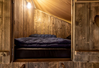 Gezellige slaapruimte in een houten glamping lodge van Holiday Park Duinhoeve, Nederland, sfeervol verlicht.