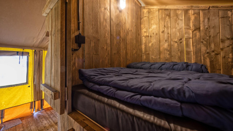 Vista interior de una acogedora tienda safari glamping con paredes de madera y cama en Holiday Park Duinhoeve, Países Bajos.