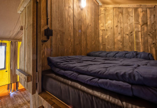 Interieur van een warme glamping safaritent met houten wanden en bed bij Holiday Park Duinhoeve, Nederland.