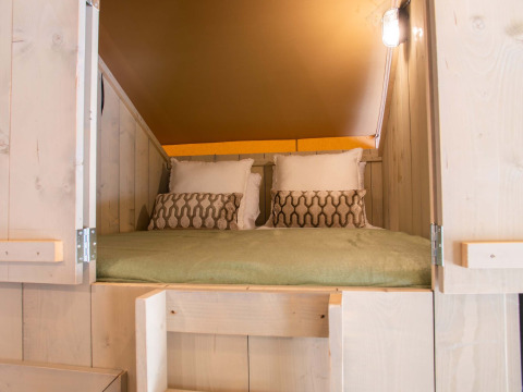 Cama acogedora dentro de una tienda safari con paredes de madera en Holiday Park Gelloo, Países Bajos.