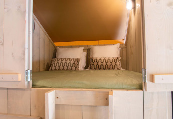 Knus bed in een safaritent met houten wanden en kussens bij Holiday Park Gelloo, Nederland.