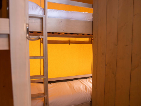 Stapelbedden in een safaritent op Vakantiepark Gelloo in Nederland, met houten muren en oranje achtergrond.