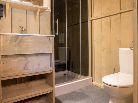 Salle de bains avec murs en bois, douche, toilettes et lavabo dans une tente safari à Holiday Park Gelloo.