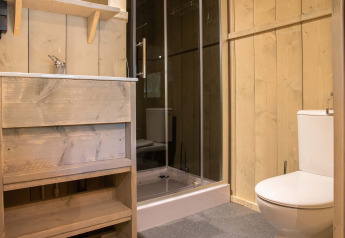 Bagno con pareti in legno, doccia, wc e lavandino in una tenda safari a Holiday Park Gelloo, Paesi Bassi.