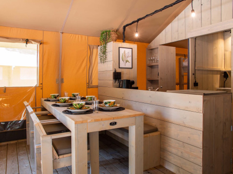 Mesa de comedor y cocina dentro de una tienda safari en Holiday Park Gelloo, Países Bajos, con interior de madera.