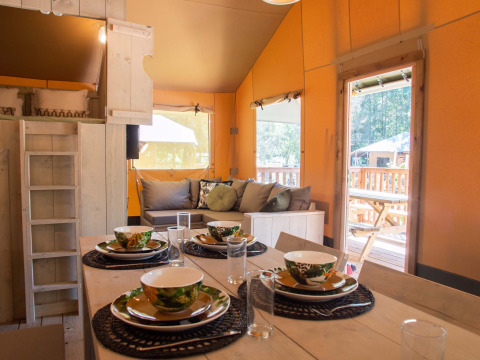 Intérieur chaleureux d'une tente safari avec table dressée et salon au Holiday Park Gelloo, Pays-Bas.