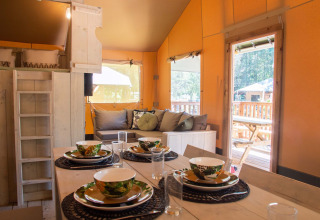 Accogliente interno di tenda safari con tavolo apparecchiato e zona salotto a Holiday Park Gelloo, Paesi Bassi.