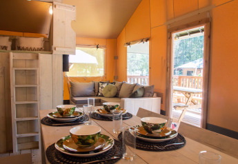 Accogliente interno di tenda safari con tavolo apparecchiato e zona salotto a Holiday Park Gelloo, Paesi Bassi.