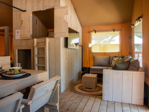 Intérieur d'une tente safari au Holiday Park Gelloo aux Pays-Bas, avec mobilier en bois et coin salon.