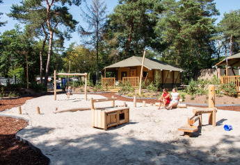 Safari-Zelt im Holiday Park Gelloo, Niederlande, mit Sandspielplatz und Familien, umgeben von Bäumen.