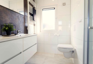 Salle de bain moderne avec WC suspendu, grande fenêtre, lavabo et plante verte au Z Module Wellness, Pays-Bas.