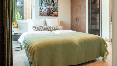 Knusse lodge-slaapkamer met tweepersoonsbed, groene deken, hertenfoto boven het bed en modern interieur.