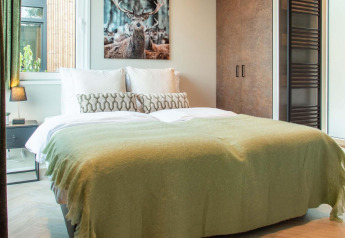 Knusse lodge-slaapkamer met tweepersoonsbed, groene deken, hertenfoto boven het bed en modern interieur.