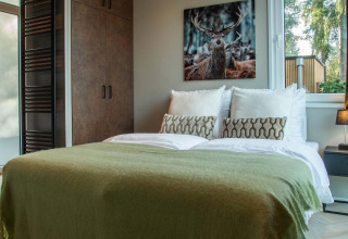 Chambre de lodge avec lit double, couverture verte, table de nuit et tableau de cerf au mur.