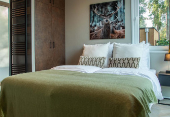 Lodge slaapkamer met tweepersoonsbed, groene deken, nachtkastje en hertenschilderij aan de muur.