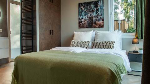 Chambre de lodge avec lit double, couverture verte, table de nuit et tableau de cerf au mur.