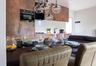 Comedor moderno en una lodge, cocina abierta, mesa puesta, lámparas de cristal y sillas acolchadas.