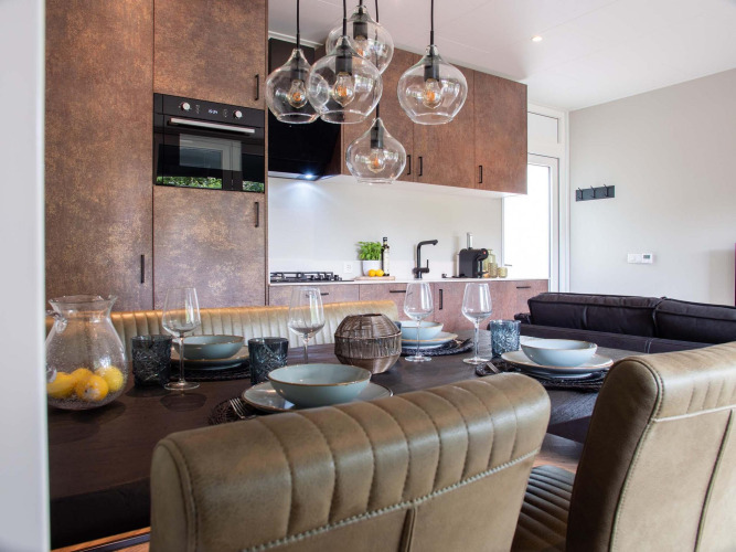 Comedor moderno en una lodge, cocina abierta, mesa puesta, lámparas de cristal y sillas acolchadas.